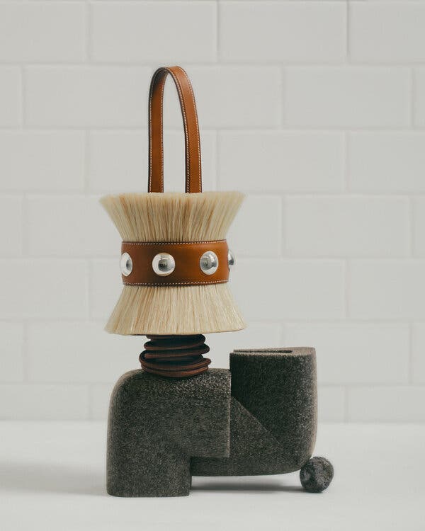 A bag with a brush-like top and base, bound together with a brown leather strap with metallic studs.